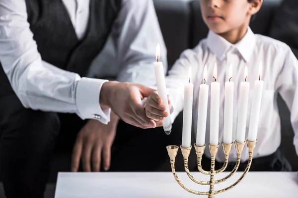 Cropped view of jewish father and son holding candle in apartment — Stock Photo