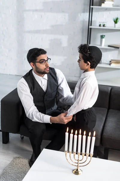 Visão de alto ângulo de pai judeu e filho bonito falando e de mãos dadas no apartamento — Fotografia de Stock