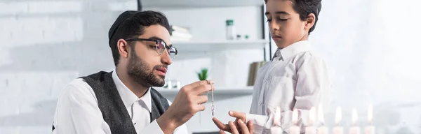 Panoramic shot of jewish father giving necklace to cute son in apartment — Stock Photo