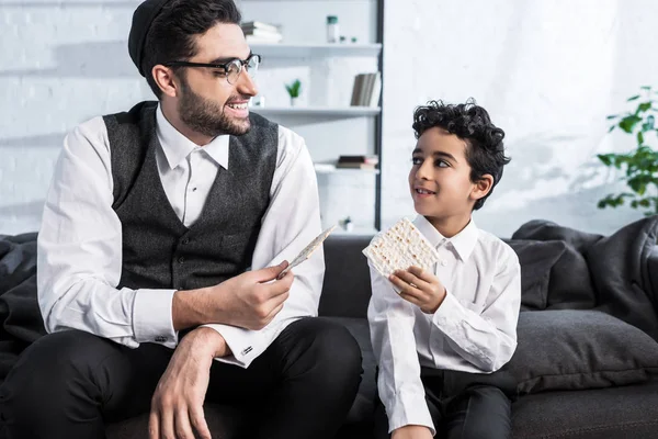 Padre e figlio ebreo sorridente che tengono Matza in appartamento — Foto stock