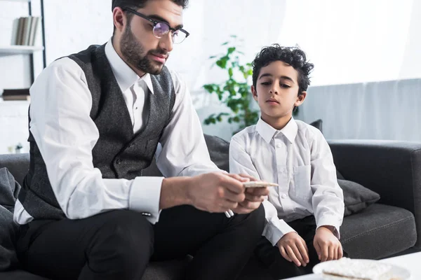 Jüdischer Vater hält Matza in der Hand und Sohn sieht es sich in Wohnung an — Stockfoto