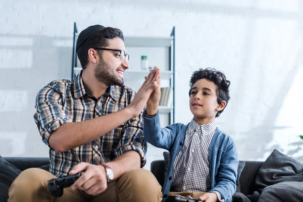 KYIV, UKRAINE - OCTOBER 15, 2019: smiling jewish father holding joystick and giving high five to son — Stock Photo