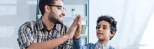 Panoramic shot of smiling jewish father giving high five to cute son — Stock Photo