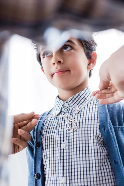 Cropped view of jewish father wearing star of david necklace on son in apartment — Stock Photo