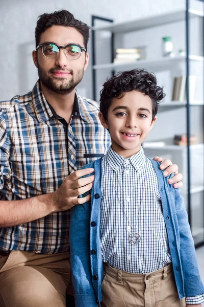 Smiling jewish father hugging son and looking at camera in apartment — Stock Photo