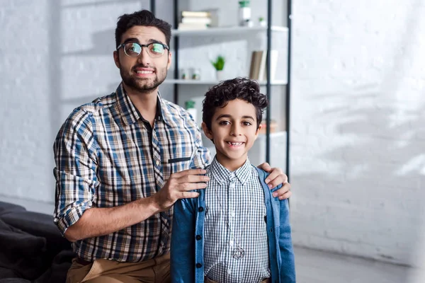 Sonriente padre judío abrazando hijo y mirando a la cámara en el apartamento - foto de stock