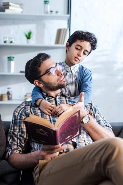 Jewish father holding tanakh and talking with son in apartment — Stock Photo