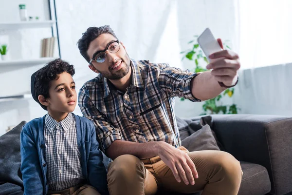 Smiling jewish father taking selfie with cute son in apartment — Stock Photo