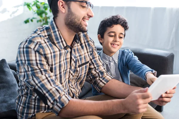 Sonrientes padre e hijo judíos usando tableta digital en el apartamento - foto de stock