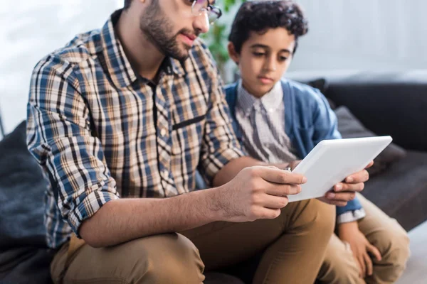 Vista recortada de padre e hijo judíos usando tableta digital en apartamento - foto de stock