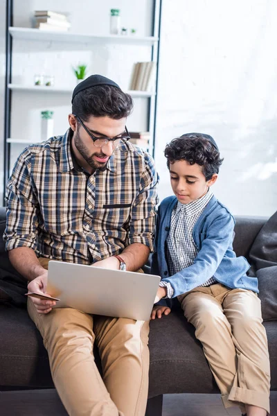 Padre judío y lindo hijo usando portátil en apartamento - foto de stock