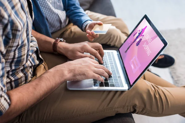 Visão cortada do pai judeu usando laptop com site de compras on-line e filho segurando cartão de crédito — Fotografia de Stock