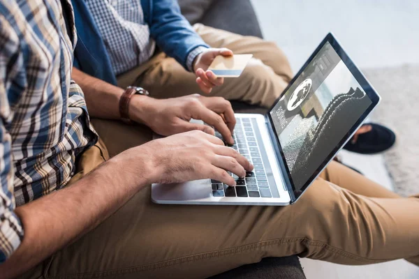 Visão cortada do pai judeu usando laptop com site de reserva e filho segurando cartão de crédito — Fotografia de Stock