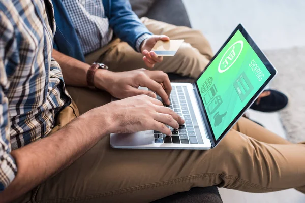 Vista recortada del padre judío utilizando el ordenador portátil con el sitio web de compras y el hijo con tarjeta de crédito - foto de stock