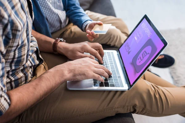 Vista recortada de padre judío usando el ordenador portátil con el Web-sitio de compras y el hijo que sostiene la tarjeta de crédito - foto de stock