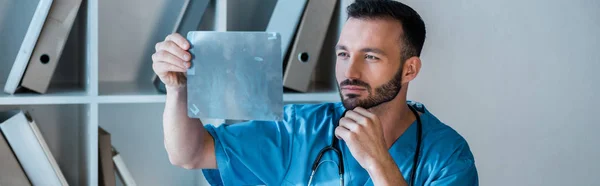 Panoramic shot of handsome orthopedist looking at x-ray — Stock Photo