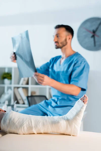 Selective focus injured woman near handsome doctor holding x-ray — Stock Photo