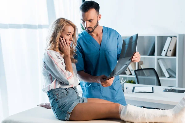 Ortopedista guapo y mujer sorprendida mirando rayos X - foto de stock