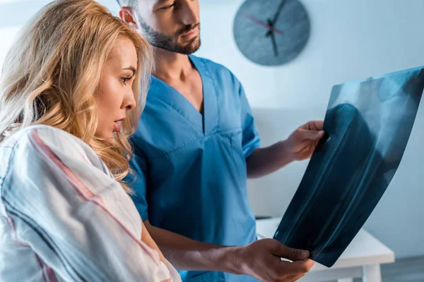 Femme choquée et médecin barbu regardant la radiographie — Photo de stock