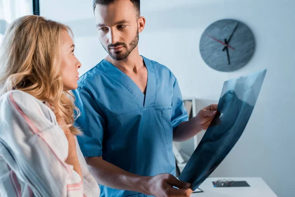 Mujer disgustada mirando al ortopedista barbudo con rayos X - foto de stock