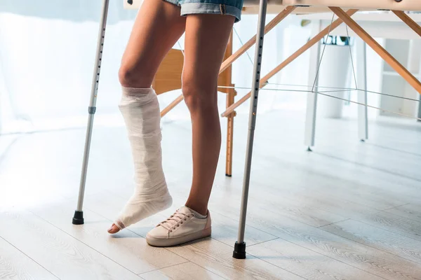Обрезанный вид перелома женщины с помощью костылей стоять в клинике — стоковое фото