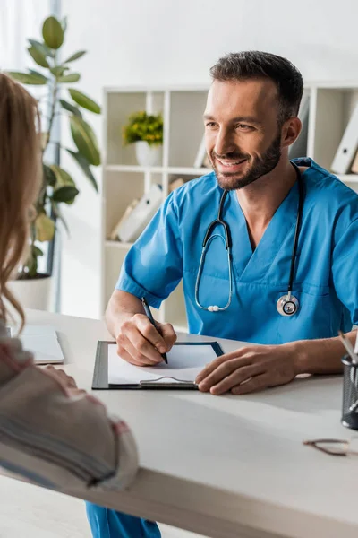 Messa a fuoco selettiva del medico felice che tiene la penna e guarda la donna — Foto stock