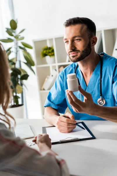 Selektiver Fokus des gutaussehenden Arztes, der Flasche mit Pillen in der Nähe der Frau hält — Stockfoto