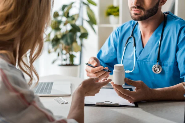 Vista ritagliata del medico barbuto bottiglia con pillole vicino alla donna — Foto stock