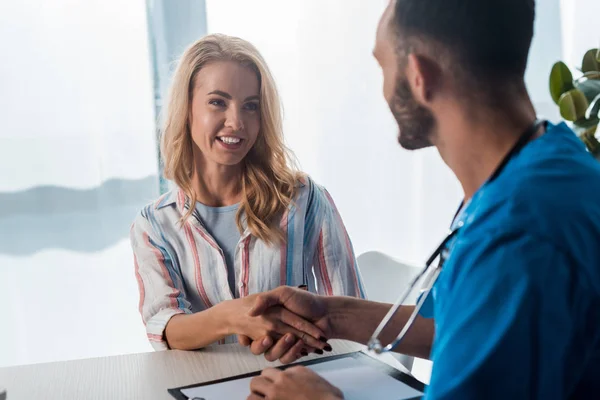 Selective focus of cheerful woman shaking hands with bearded doctor in clinic — Stock Photo