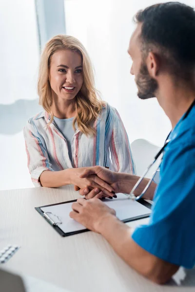 Foyer sélectif de femme souriante serrant la main avec un médecin barbu à la clinique — Photo de stock