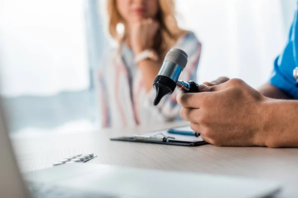 Cropped view of doctor holding otoscope near woman in clinic — Stock Photo
