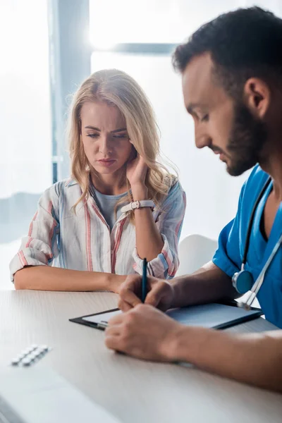 Enfoque selectivo de la mujer triste sentado cerca de médico escribir prescripción - foto de stock