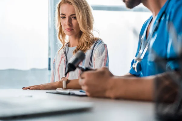 Selective focus of attractive woman looking at otoscope in hands of doctor — Stock Photo