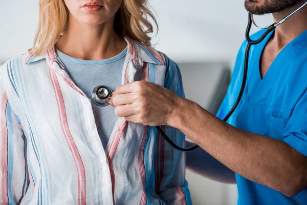 Ausgeschnittene Ansicht eines bärtigen Arztes, der Frau mit Stethoskop untersucht — Stockfoto