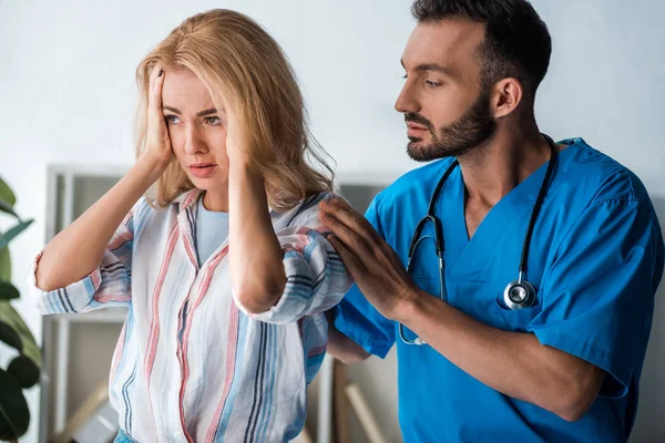Guapo doctor tocando emocional mujer con dolor de cabeza - foto de stock