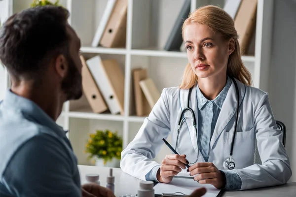 Selective focus of attractive doctor looking at man in clinic — Stock Photo