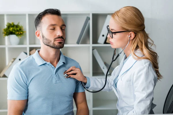 Attraente medico in occhiali esaminando bello uomo con gli occhi chiusi — Foto stock