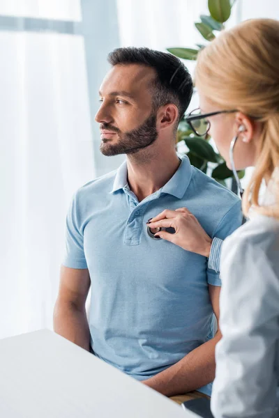 Selective focus of doctor in glasses examining handsome man — Stock Photo