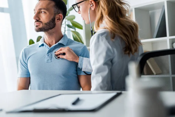 Enfoque selectivo del médico en gafas que examinan hombre barbudo guapo - foto de stock