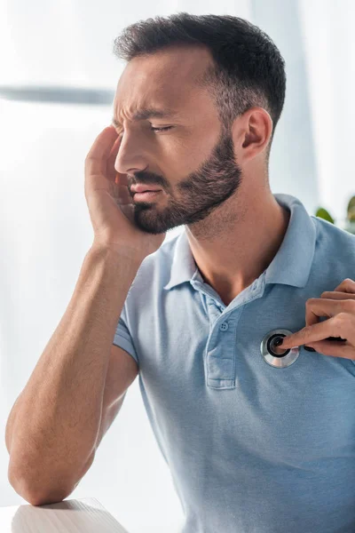 Vista recortada del médico examinando al hombre barbudo con dolor de cabeza - foto de stock
