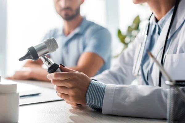 Cropped view of doctor holding otoscope near man in clinic — Stock Photo