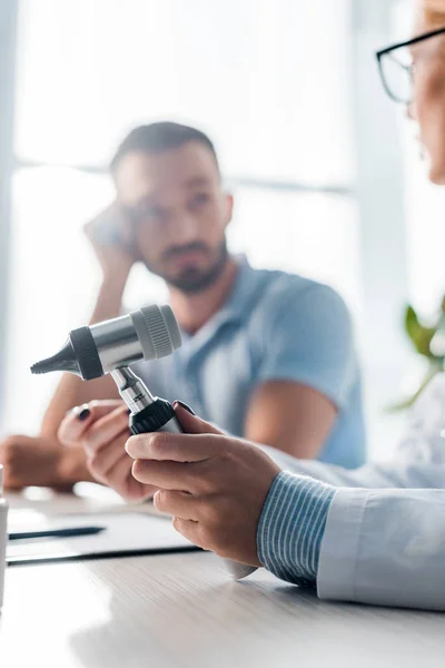 Selective focus of doctor in glasses holding otoscope near handsome man in clinic — Stock Photo