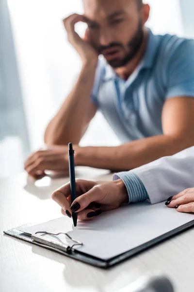 Messa a fuoco selettiva del medico scrittura prescrizione vicino uomo triste — Foto stock