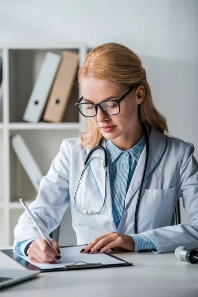 Hermoso médico en gafas escribir diagnóstico en la clínica - foto de stock