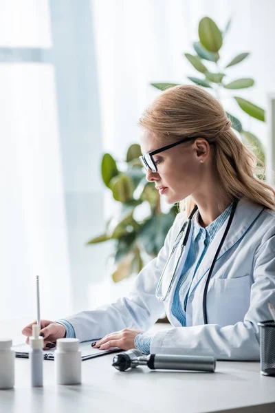 Attractive doctor in glasses writing diagnosis in clinic — Stock Photo