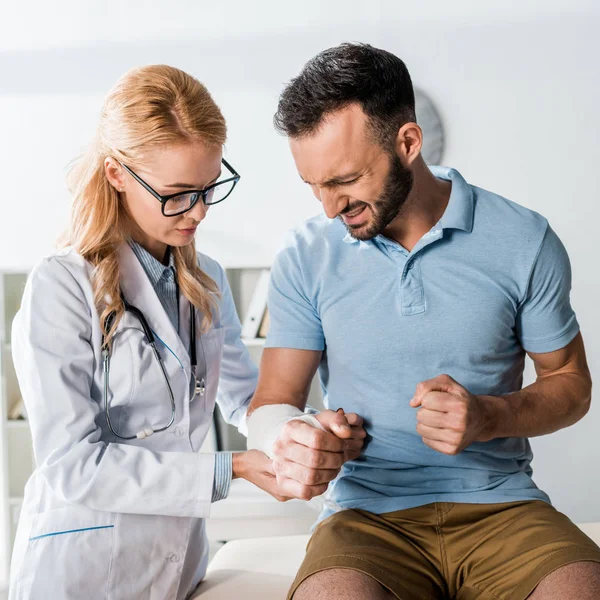 Attractive orthopedist touching injured arm of man — Stock Photo