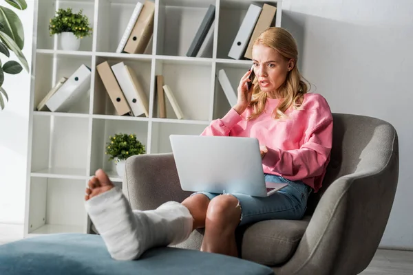 Injured woman talking on smartphone while working from home — Stock Photo