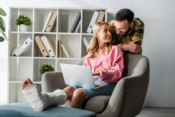 Bärtiger Mann nähert sich verletzter Frau, die von zu Hause aus mit Laptop arbeitet — Stockfoto