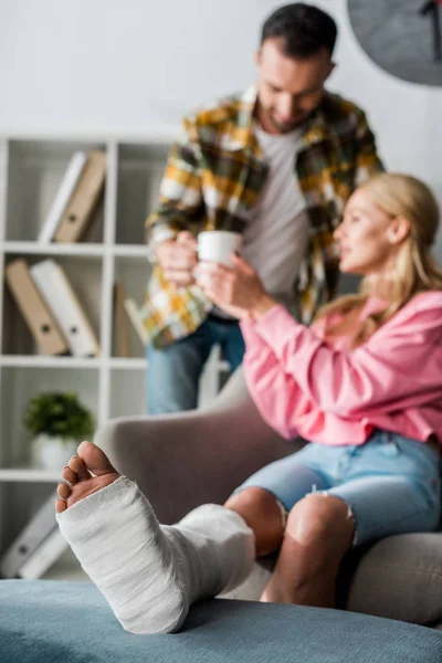 Verletzte Frau nahe gutaussehendem Mann mit Tasse Tee im Fokus — Stockfoto