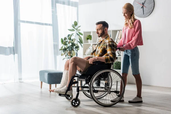 Веселая женщина, стоящая рядом с бородатым мужчиной, сидящим в инвалидном кресле — стоковое фото